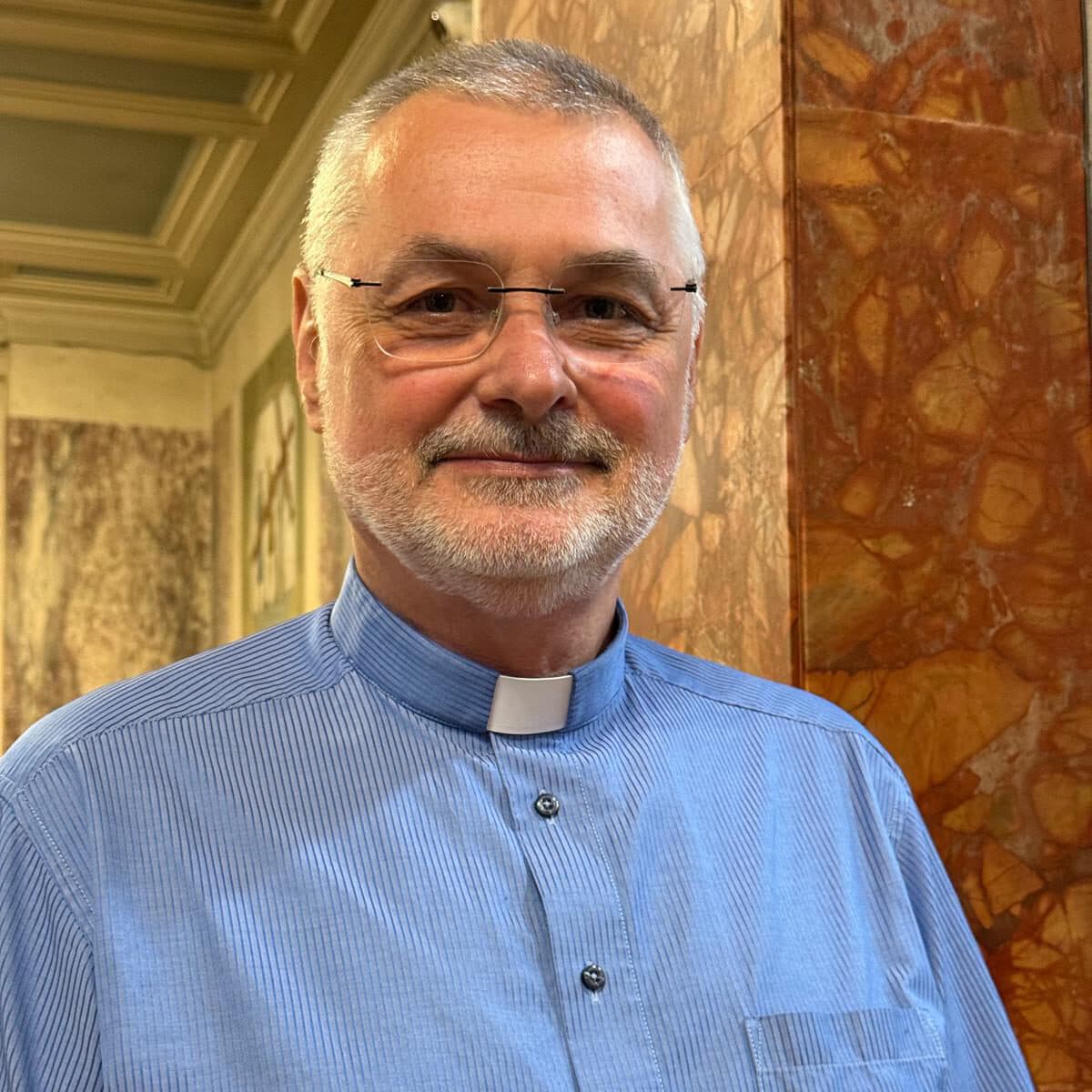 Fr Krzysztof Krzyskow, Parish Priest, smiling in a blue clerical shirt inside St Saviour's Church
